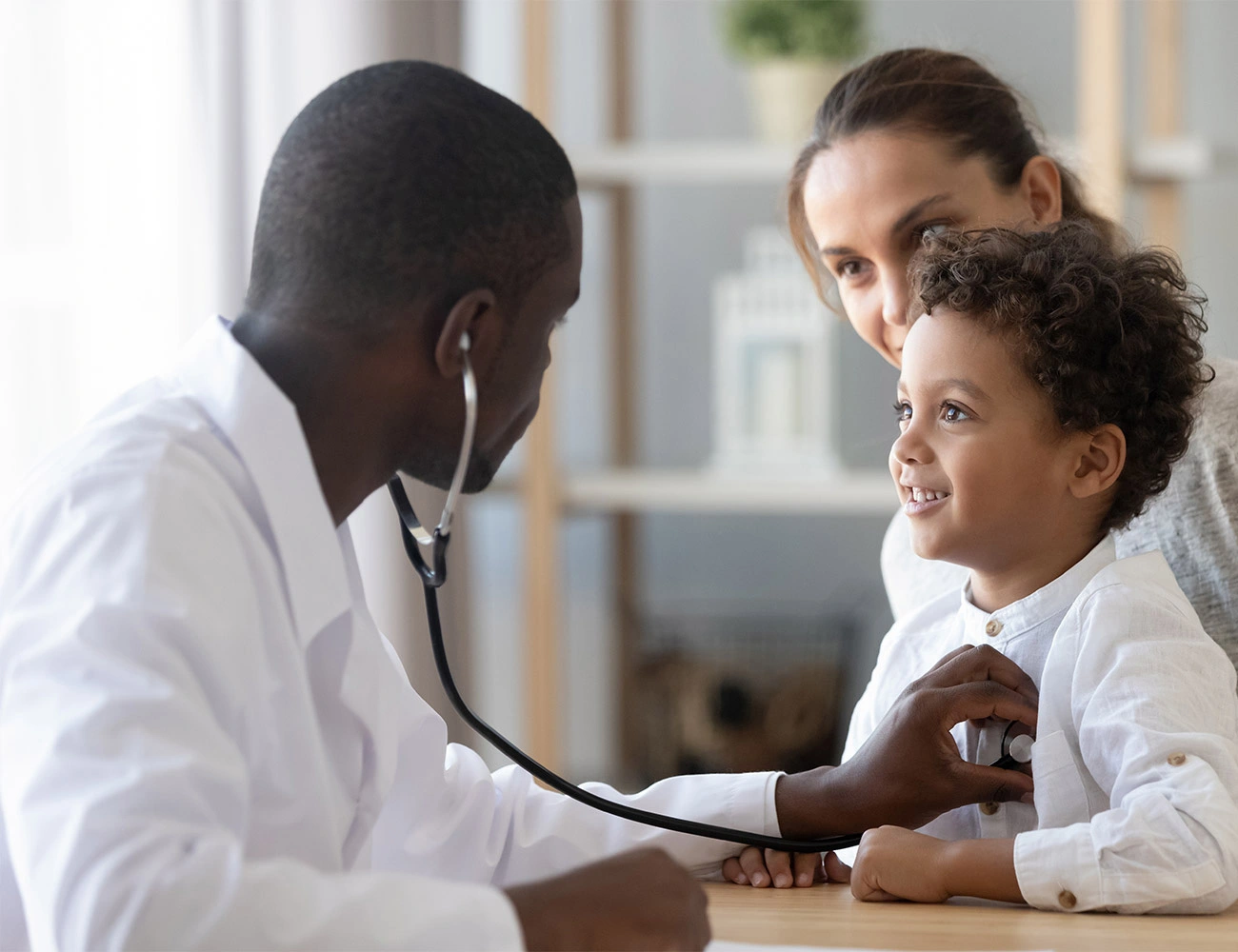 一位年轻的黑人医生用听诊器听诊小男孩的肺部，小男孩的母亲在一旁观看。