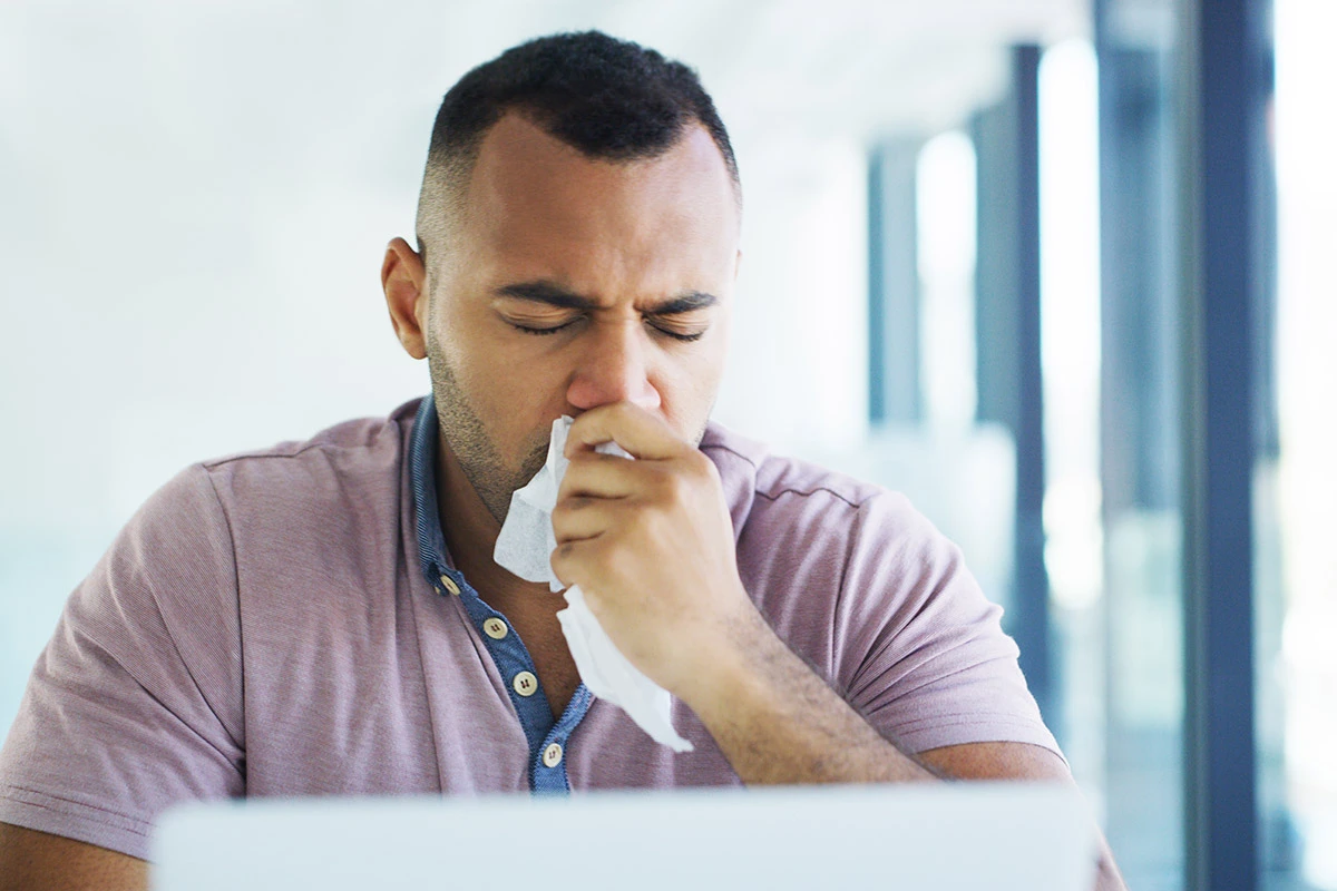 Man coughing into tissue at his desk